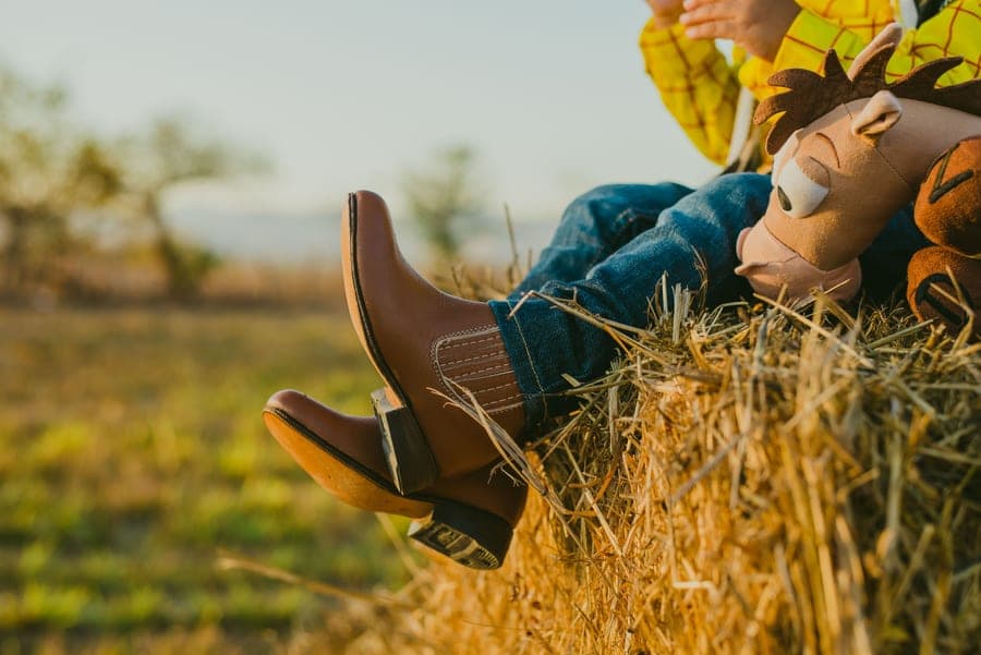 A child wearing western boots sitting on a hay bale
